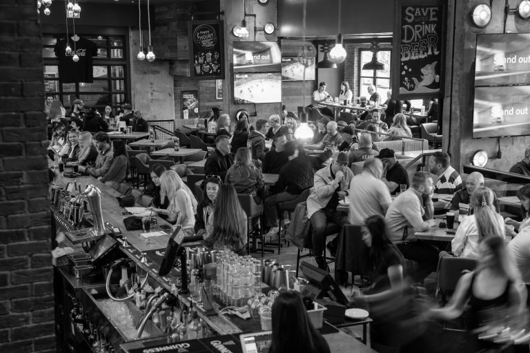 A crowd of people sitting around closely spaced tables, as well as at the bar